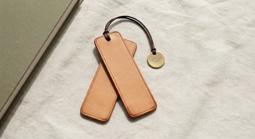 Marque-page artisanal en cuir et plaque de laiton gravée d'un symbole Ichthys, posés sur un lin crème froissé