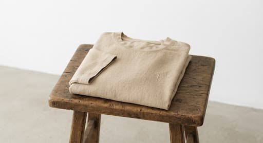 T-shirt de lin organique soigneusement plié sur un tabouret de bois brut, texture naturelle du tissu révélée par une lumière douce